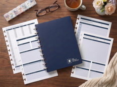 The Caregiver Kit from The Perfect Notebook: navy B5 disc-bound notebook with caregiver planning refill pages, pill organizer, glasses and tea on a wooden desk